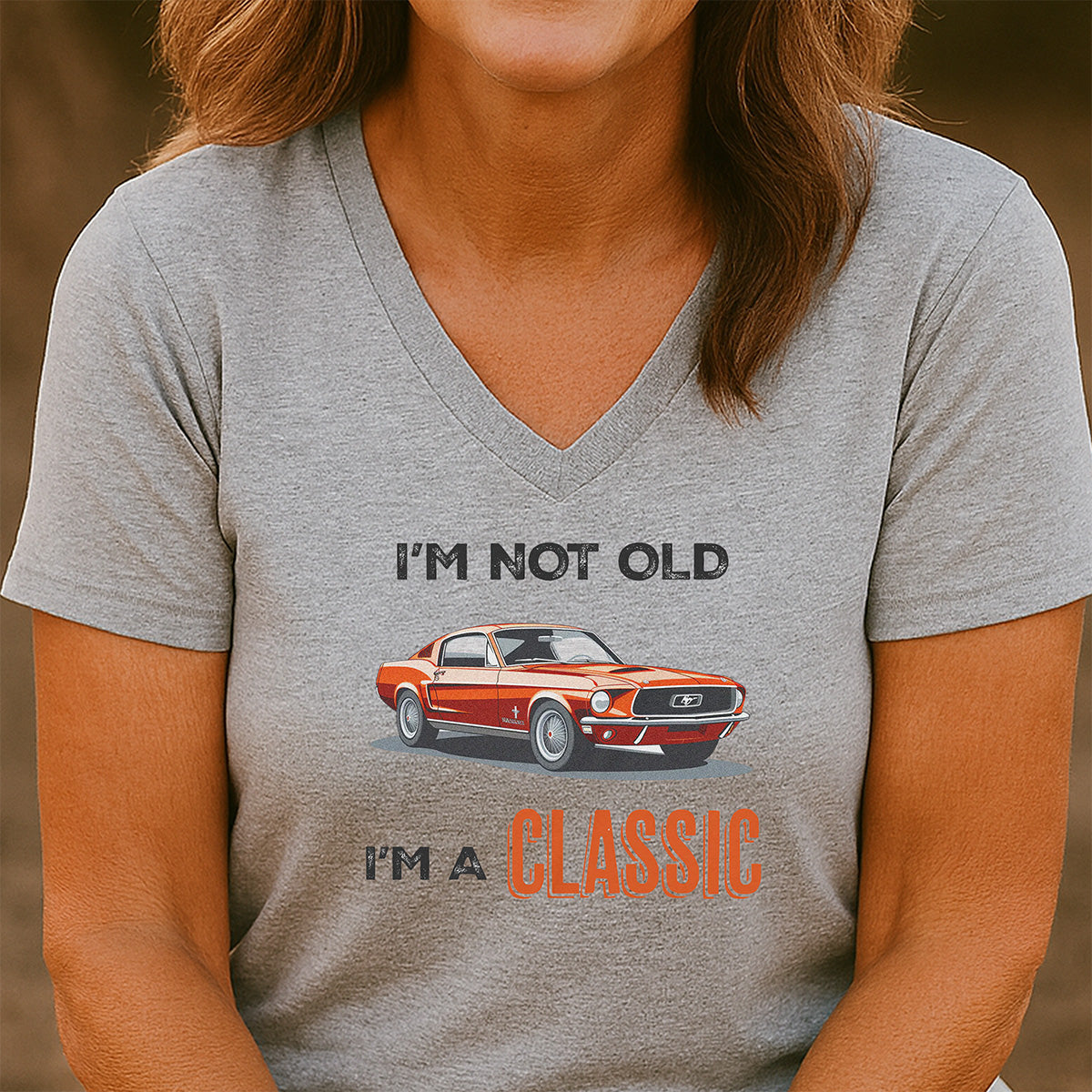Woman wearing gray V-neck T-shirt with orange classic car graphic and I’m not old I’m a classic slogan