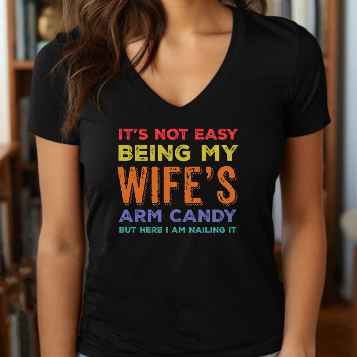 Woman in black v-neck shirt with colorful text it's not easy being my wife's arm candy but here I am nailing it